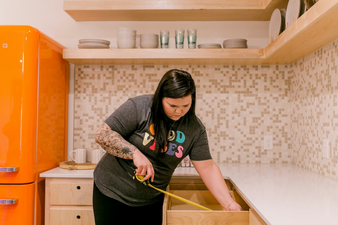 A woman measures a kitchen drawer with a tape measure